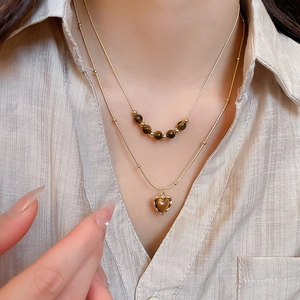 Close-up of double-layer gold necklace featuring tiger eye beads and heart pendant