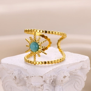 Detailed shot of gold sun motif ring with turquoise gemstone on white stone pedestal