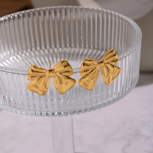 Detail shot of golden bow earrings featuring a textured pleated design on a glass rim