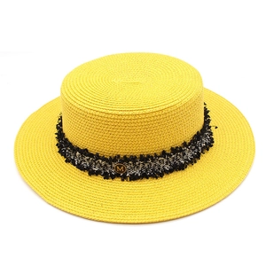 Detail of yellow straw boater hat with black and white fringe ribbon and gold M charm