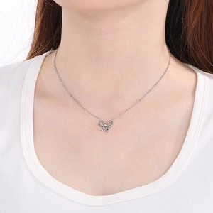 Close-up of minimalist silver bow pendant necklace worn on neck with metallic shine