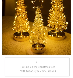 Three glowing gold metal wire Christmas trees with star toppers and LED bases on a desk
