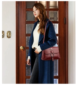Detail view of burgundy pebble leather shoulder bag with metal ring buckle on blue coat