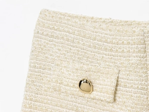 Détail du tissu en tweed crème avec fils dorés et boutons métalliques dorés irréguliers