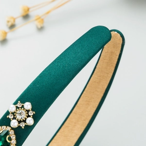 Close-up of green satin headband featuring intricate pearl and emerald floral details