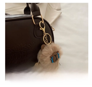 Detailed close-up of a plush animal keychain with gold ring on a dark brown handbag