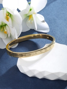 Detailed shot of golden stainless steel bangle with engraved Roman numerals on blue background