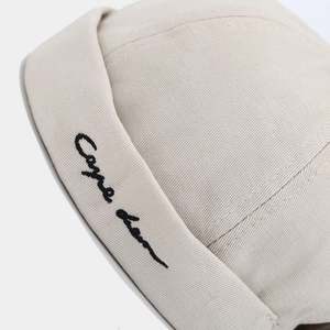 Detail of minimalist cursive embroidery on a beige cotton miki hat with twill texture