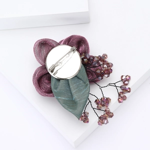 Detail of deep purple ribbon flower brooch with green plaid leaf and bead accents