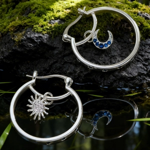 Détail de boucles d'oreilles soleil et lune avec pierres sur mousse et eau