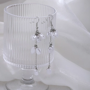 Detail of silver butterfly tassel earrings with white pearls hanging on glass