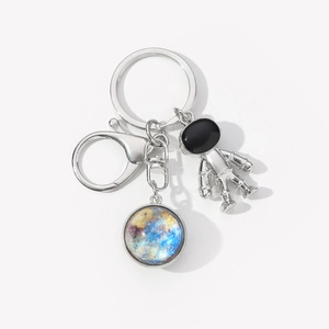 Detail of metal astronaut keychain featuring a star pattern glass pendant on white background