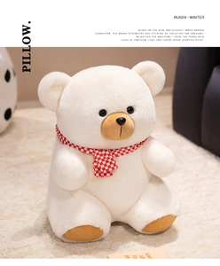 Detail of soft white plush teddy bear wearing a red checkered scarf on a cozy carpet