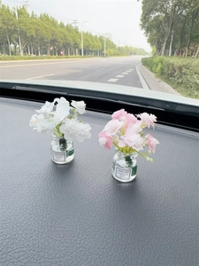 Close-up of pink and white artificial flowers in glass jars on a car dashboard