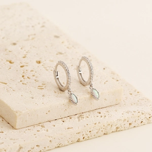 Detailed shot of S925 silver opal earrings with pavé diamonds on a stone surface