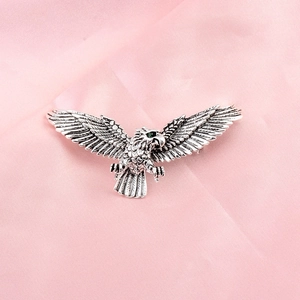 Close-up of eagle brooch with silver feather texture and green crystal eye detail