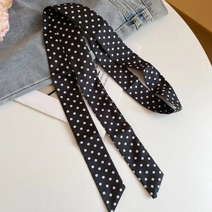 Detail of a black and white polka dot silk scarf displayed with flowers and denim