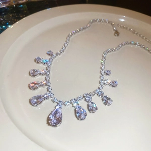 Detailed view of silver zircon tassel necklace with water drop gems on a white plate