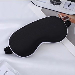 Detailed view of black faux silk sleep mask with white trim on a soft fabric background