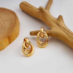 Macro detail of gold interlocking triple hoop earrings on a natural wood display