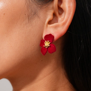 Gros plan d'une boucle d'oreille fleur rouge floquée avec centre doré sur l'oreille