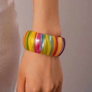 Détail d'un large bracelet en acétate avec des rayures verticales colorées sur le poignet