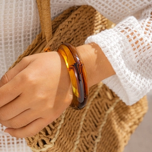 Nahaufnahme eines dicken bernsteinfarbenen Acryl-Armreifs für einen schicken Retro-Sommerlook