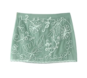 Close-up of light green mini skirt featuring white corded floral embroidery detail