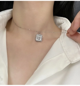Macro shot of silver butterfly square pendant on pearl chain necklace worn on neck