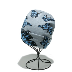 Gros plan d'un bonnet en tricot gris avec motif papillon bleu sur un support noir