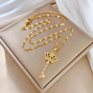 Elegant gold titanium crown key necklace with sparkling crystals on white silk background