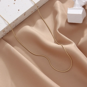 Detail of a thin gold snake bone necklace chain on champagne satin with stone texture