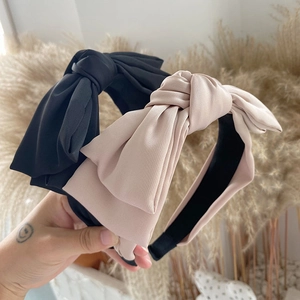 Close-up of elegant oversized satin bow headbands in black and beige silk texture