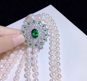 Macro shot of multi-layer pearl necklace with green gemstone flower clasp in silver