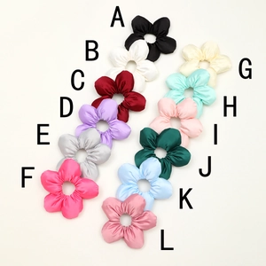 Flat lay of twelve silk flower scrunchies in various pastel colors with letter labels