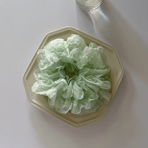 Close-up of light green organza scrunchie with layered ruffle texture on ceramic plate