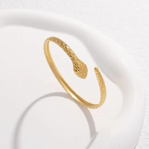 Detail of gold snake-shaped open bracelet featuring a textured diamond-cut surface design