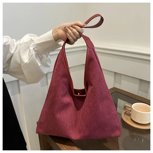 Macro shot of burgundy suede shoulder bag on a wooden table near a ceramic cup