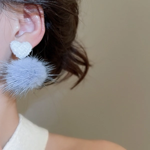 Dettaglio dell'orecchino a cuore intrecciato e ciondolo a pompon blu su modella