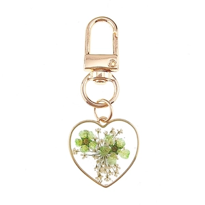Detail of a golden heart keychain with green dried flowers embedded in clear resin