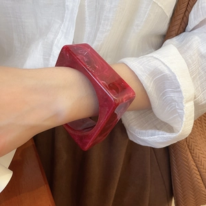Detail of square acrylic bangle with dark red marble texture worn with a white shirt
