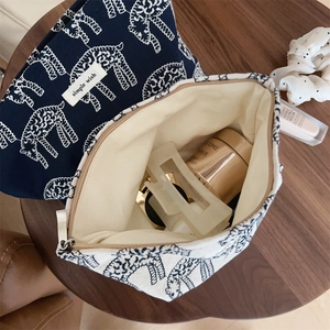Flat lay of navy and beige embroidered canvas makeup bags on a wooden table with cosmetics