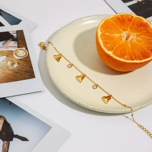 Close-up of golden heart and zircon bracelet draped over a ceramic plate with orange