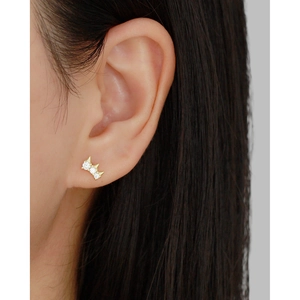 Close-up of golden crown stud earring with three white zircons worn on the earlobe