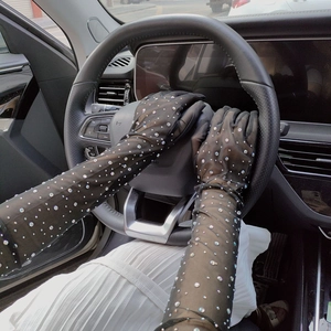 Close-up of black mesh lace gloves with rhinestones gripping a car steering wheel