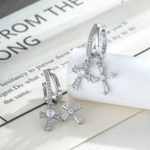 Silver cross drop earrings with clear gemstones on a minimalist vintage book background