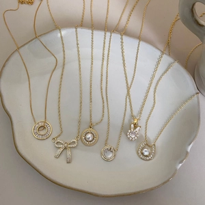 Elegant gold bow necklaces with zircon pendants on a beige ceramic display tray