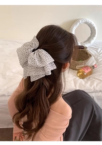 Detail of large white chiffon bow hair clip with black polka dots on model's ponytail