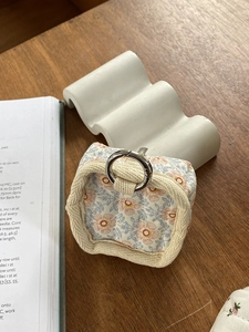 Close-up of quilted floral data cable storage pouch with metal ring on wooden desk