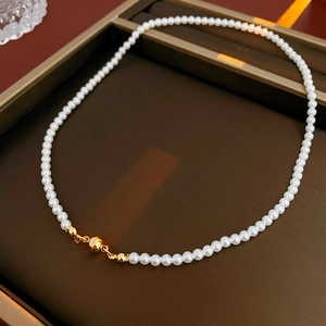 Detailed view of white pearl necklace with gold magnetic clasp on a brown tray